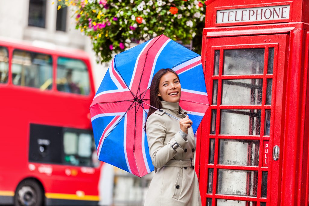 Piros telefonfülke előtt, angol zászlós esernyővel pózoló lány