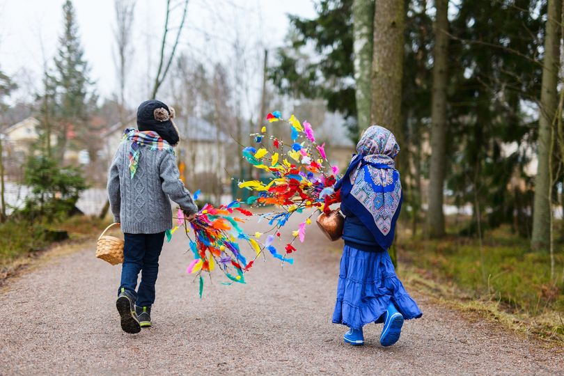 Két kisgyerek színes tollakkal díszített botokat cipel